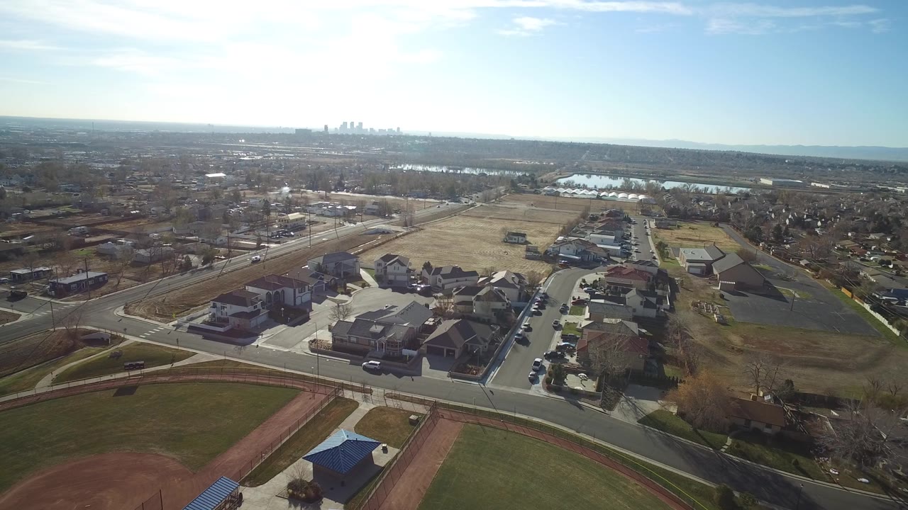 Aerial view with neighborhood streets, houses, park grass, and distant water.