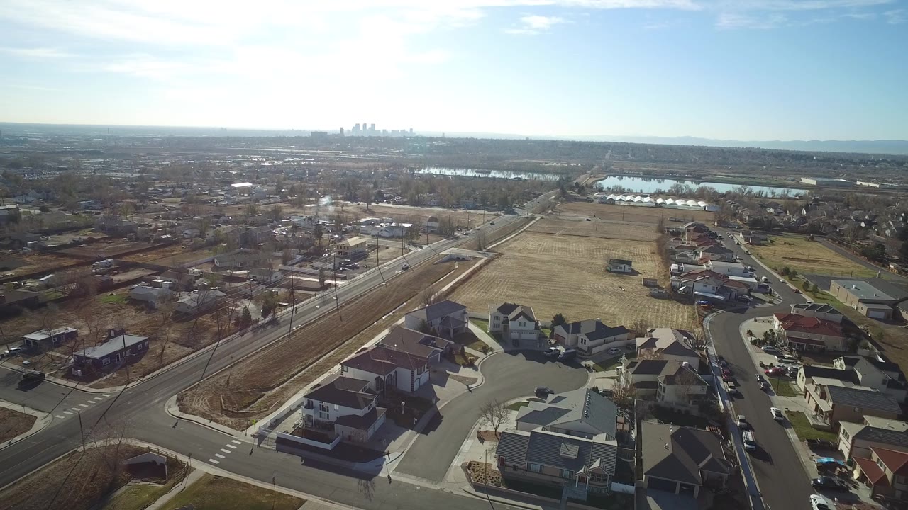 Drone-style aerial view of homes, a main road, open fields, and hazy skyline.
