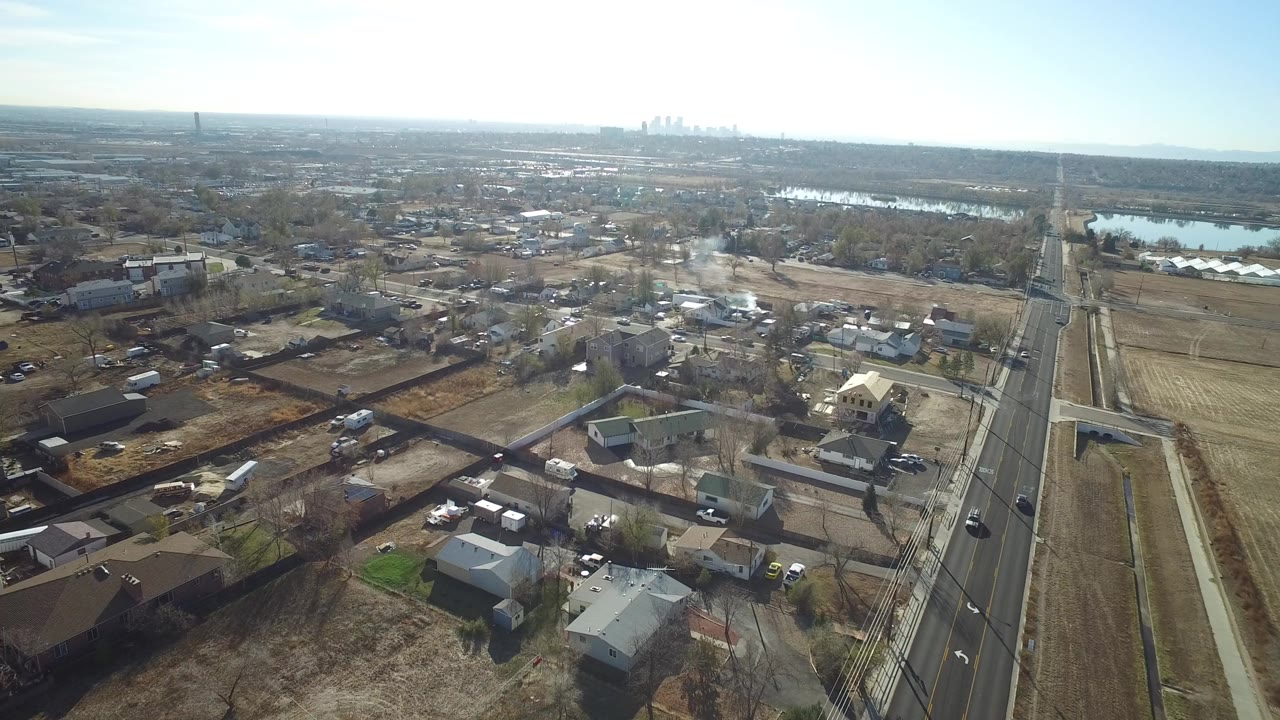 Aerial view over residential lots, road, water, and distant skyline