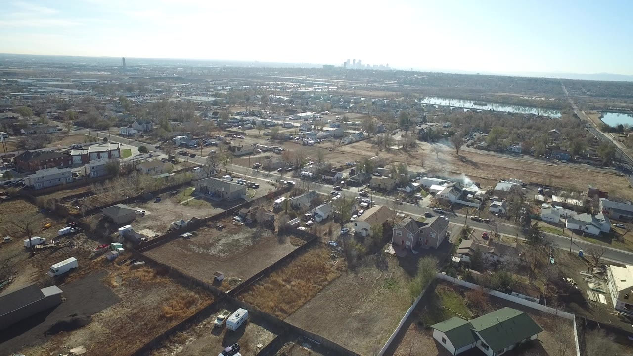 Aerial view of suburban homes, streets, open lots, and distant skyline