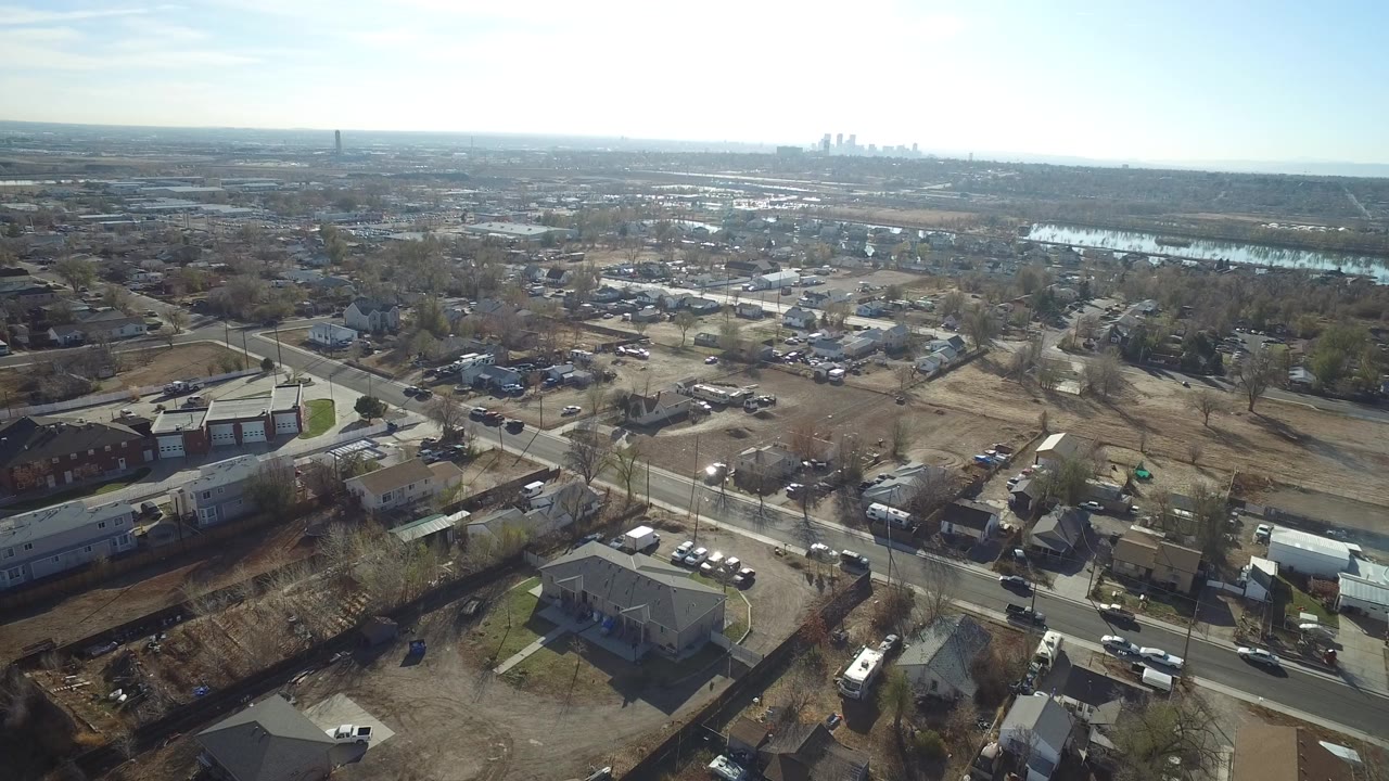 Aerial view over suburban roads, houses, trees, and distant skyline.