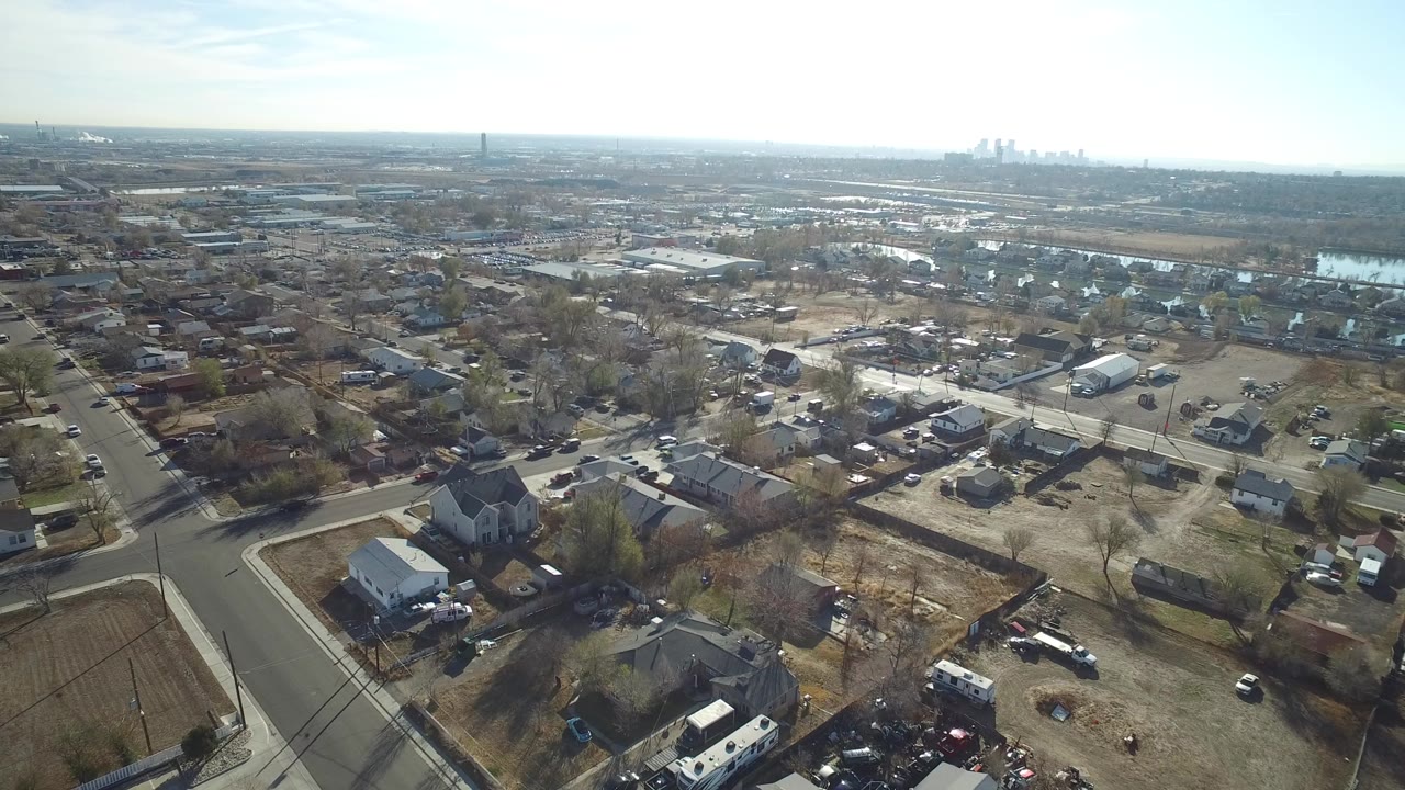 High aerial view of suburban streets, houses, bare trees, and distant skyline.