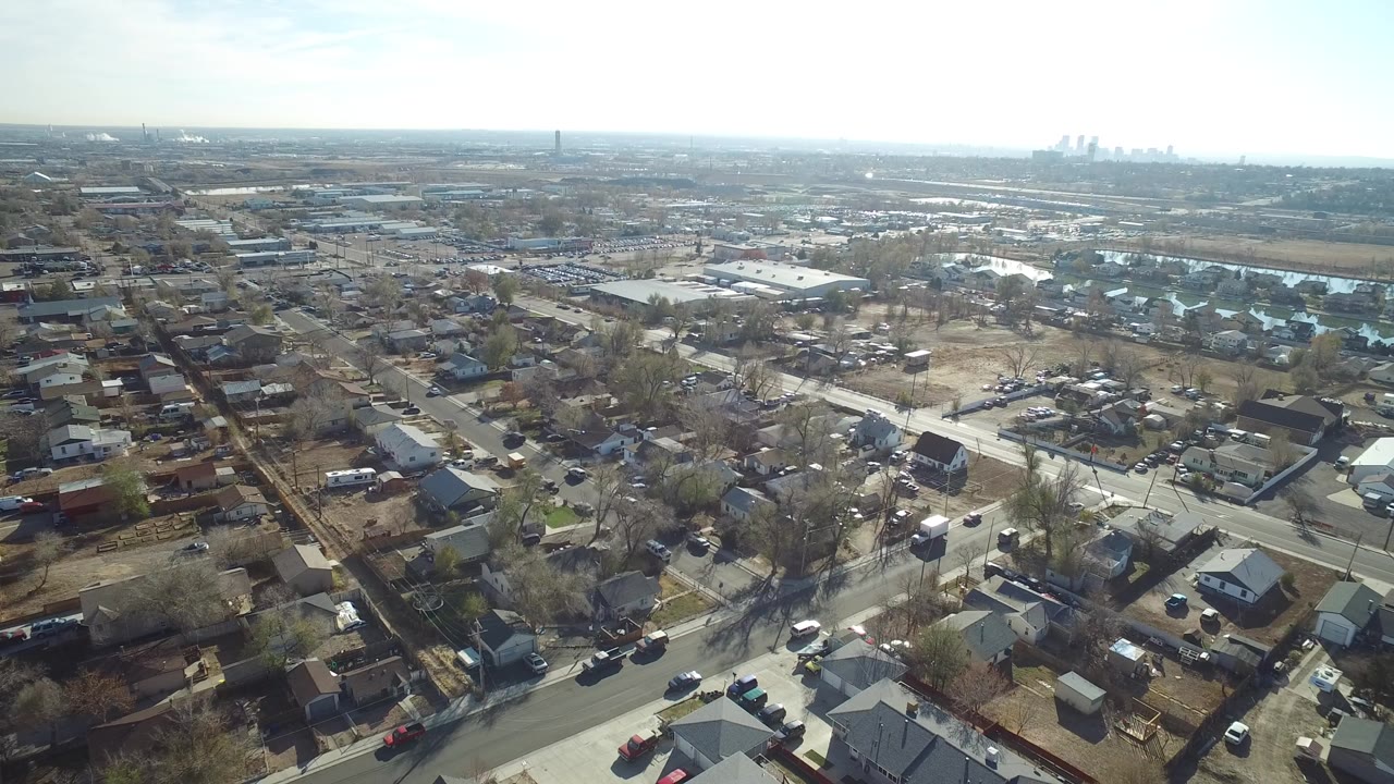 Wide aerial view over Westminster, Colorado neighborhoods with gridded streets, rooftops, bare trees, commercial roofs, a hazy horizon, and no visible people.