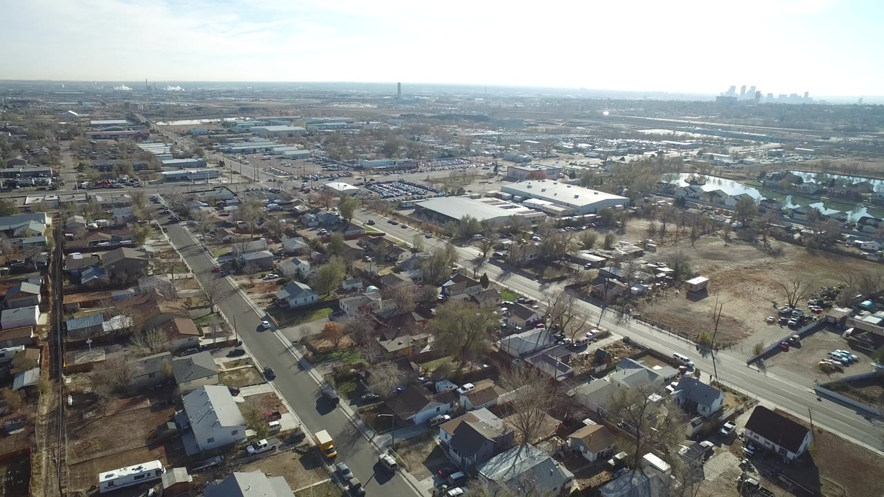 Aerial view over houses, roads, open lots, and low industrial buildings.