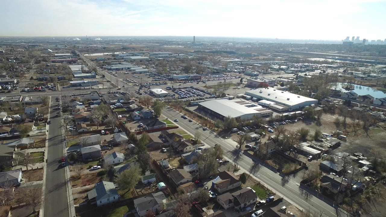 Aerial view of roads, houses, warehouses, and distant industrial stacks.