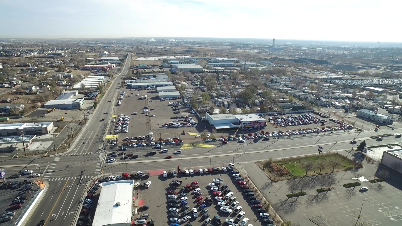High aerial frame in Westminster, Colorado showing dealership inventory, traffic lanes, parking lots, commercial buildings, and no visible people.