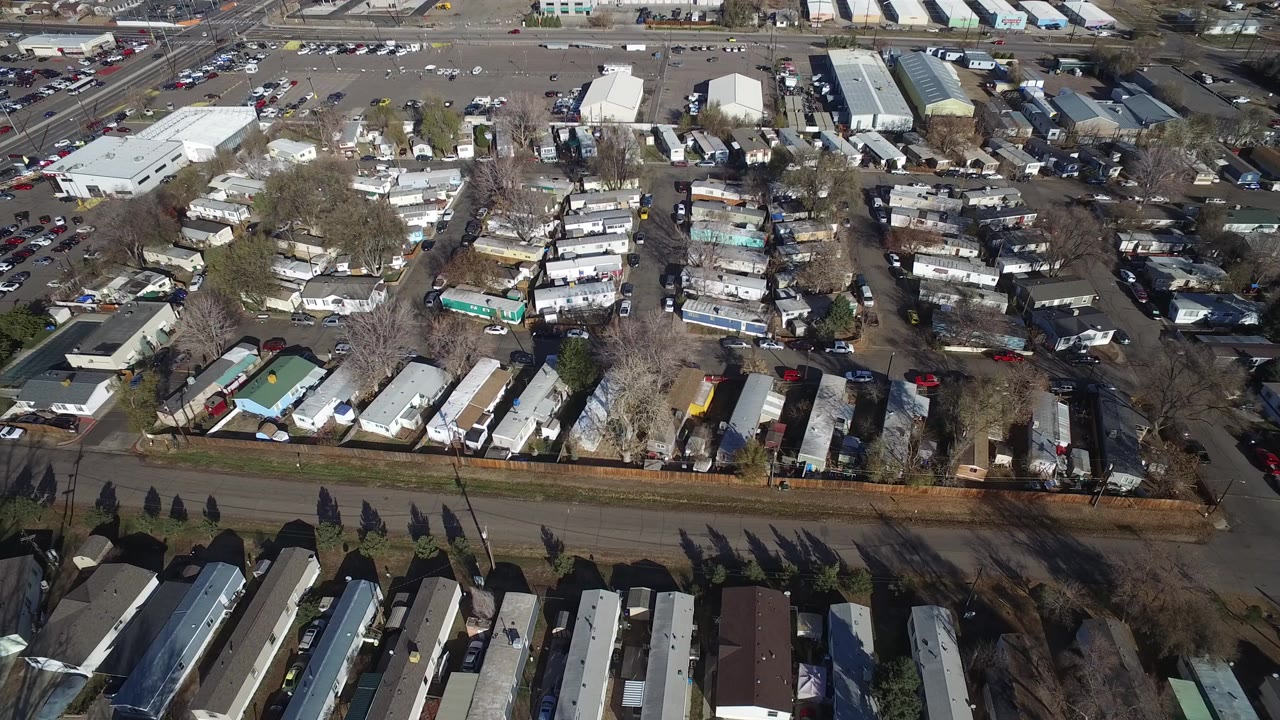 Overhead view of mobile homes, roads, parked cars, and commercial roofs.