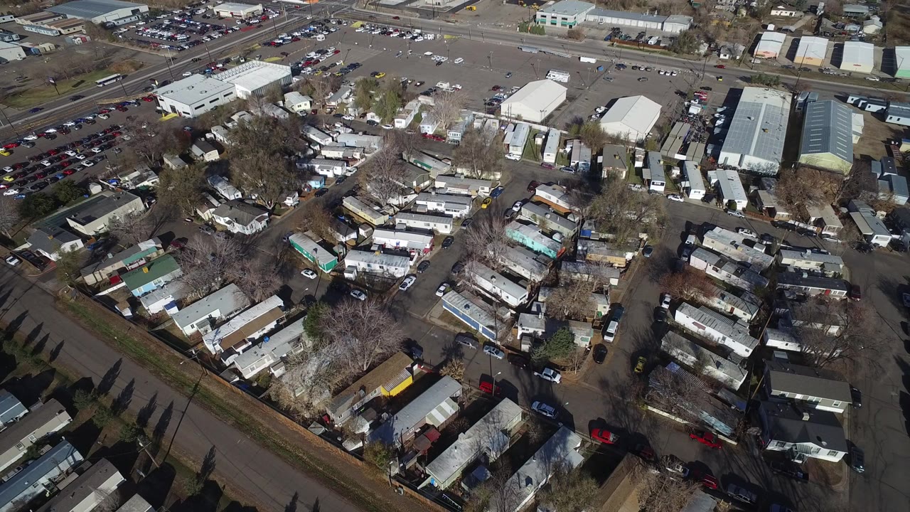 Aerial frame over Westminster, Colorado showing manufactured homes in the foreground, warehouse buildings and parking lots beyond, and no visible people.