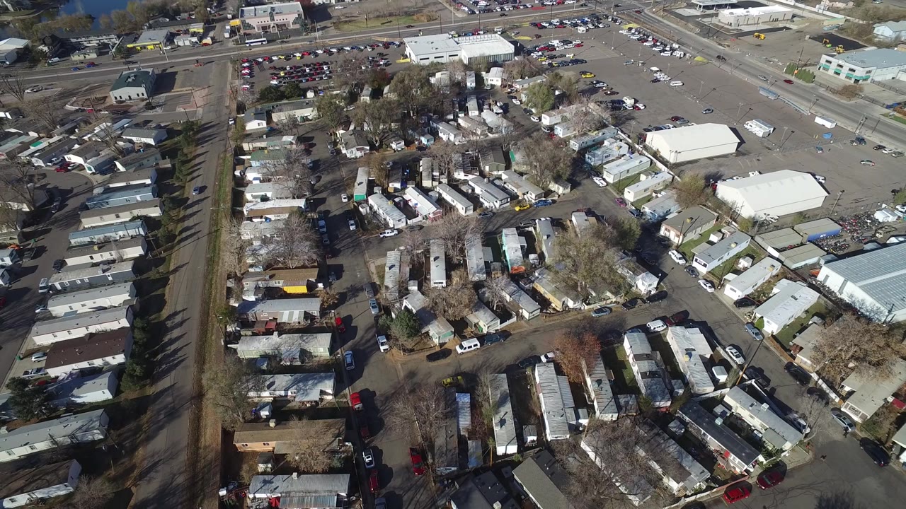 Aerial neighborhood view with mobile homes, parked cars, and wide parking lots.