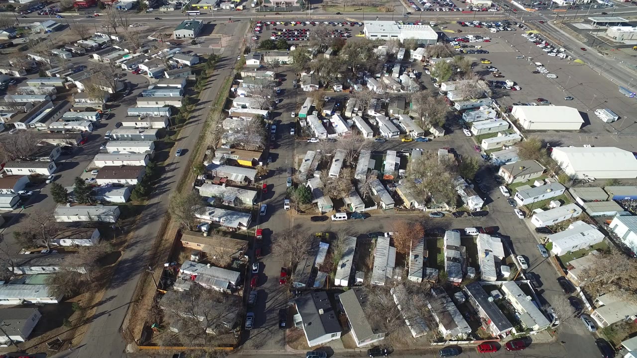 High aerial frame over Westminster, Colorado showing rows of trailers, small buildings, paved roads, parked cars, bare trees, and no visible people.