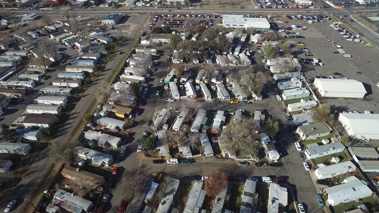Aerial view in Westminster, Colorado with the residential rows centered, a large pale commercial building at right, parking lots beyond, and no visible people.