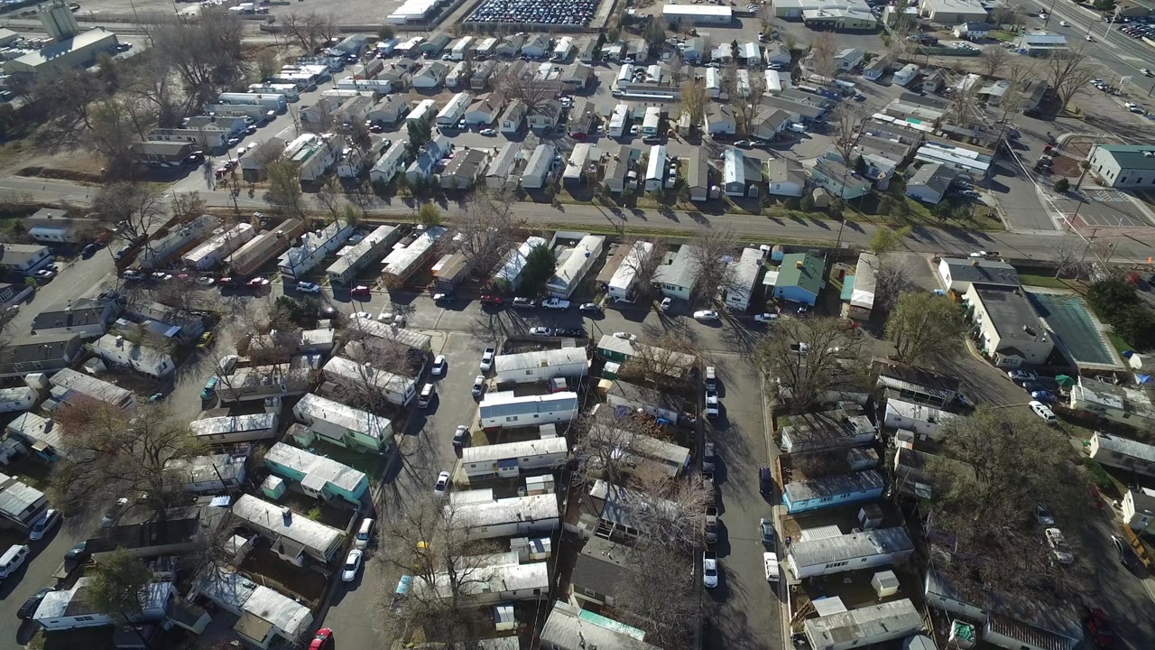 A second overhead frame in Westminster, Colorado centers on rows of mobile homes and narrow streets, with parked vehicles, leafless trees, and larger buildings at the top edge, with no visible people.