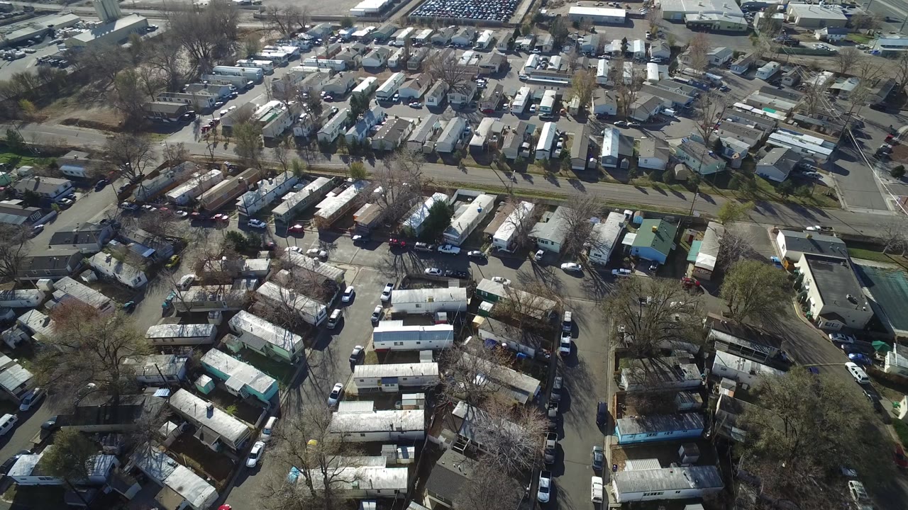 High overhead neighborhood view with rooftops, curving roads, parked cars, trees, and a parking area in the distance.