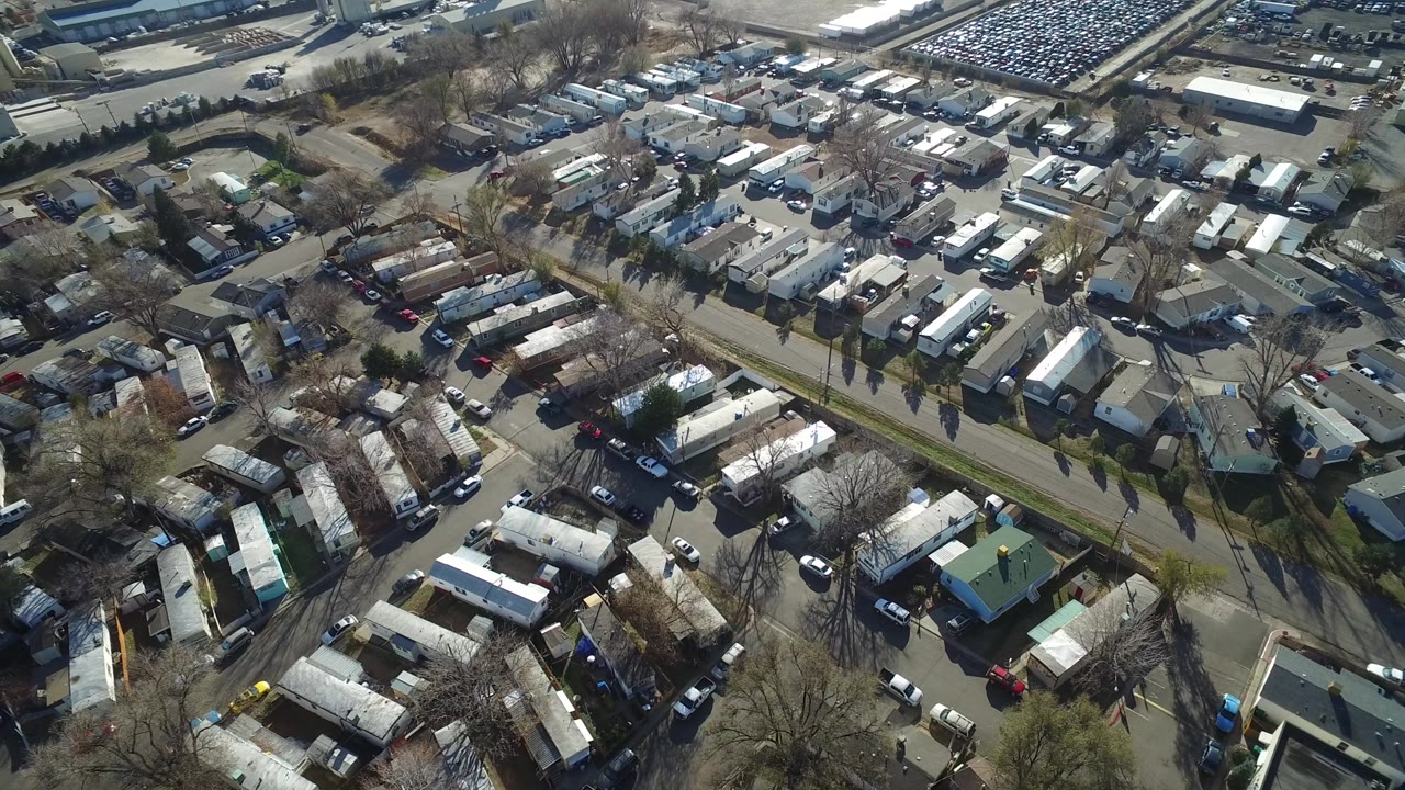 Oblique aerial view of mobile homes, roads, trees, and parked cars.