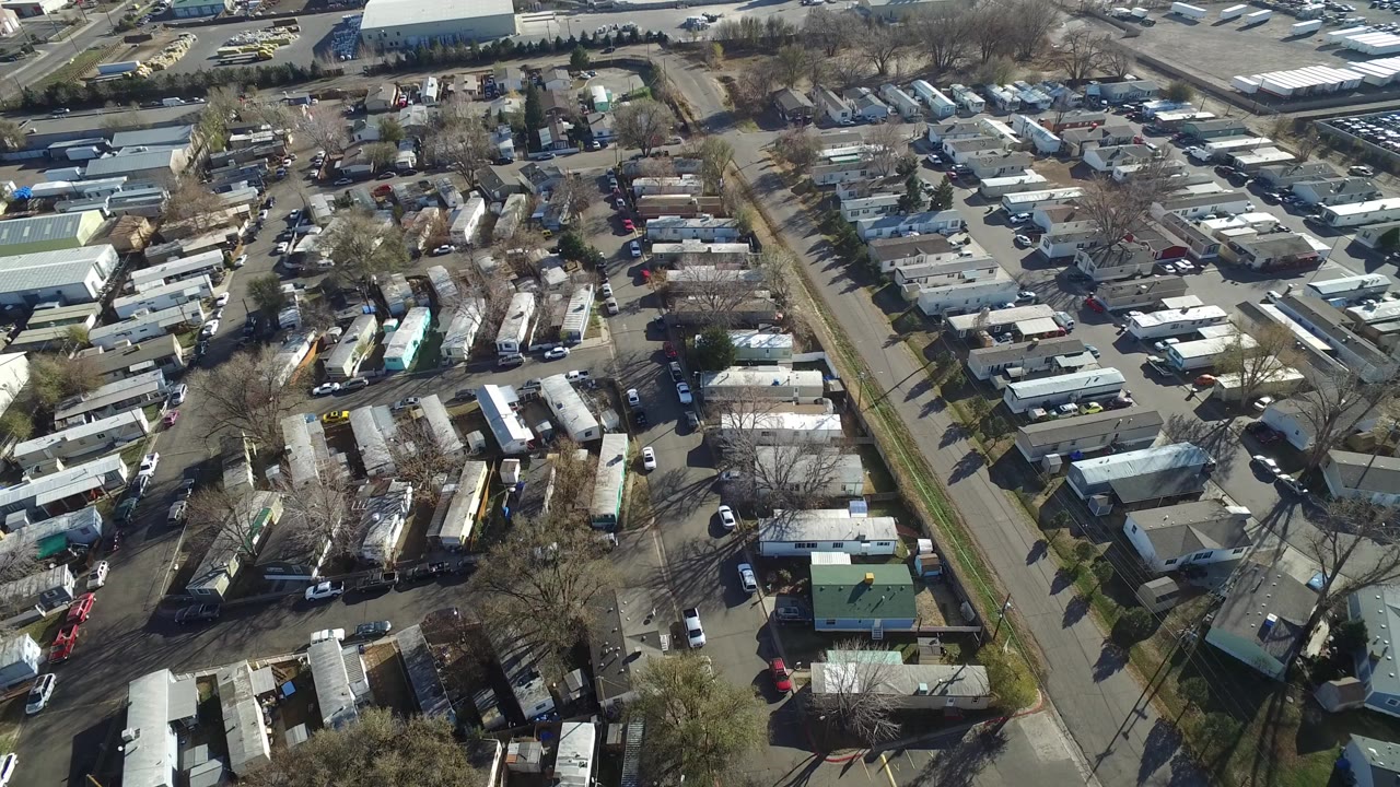 High aerial view over Westminster, Colorado, showing compact residential lots, small homes, parked vehicles, a broad street, and no visible people at the start of the clip.