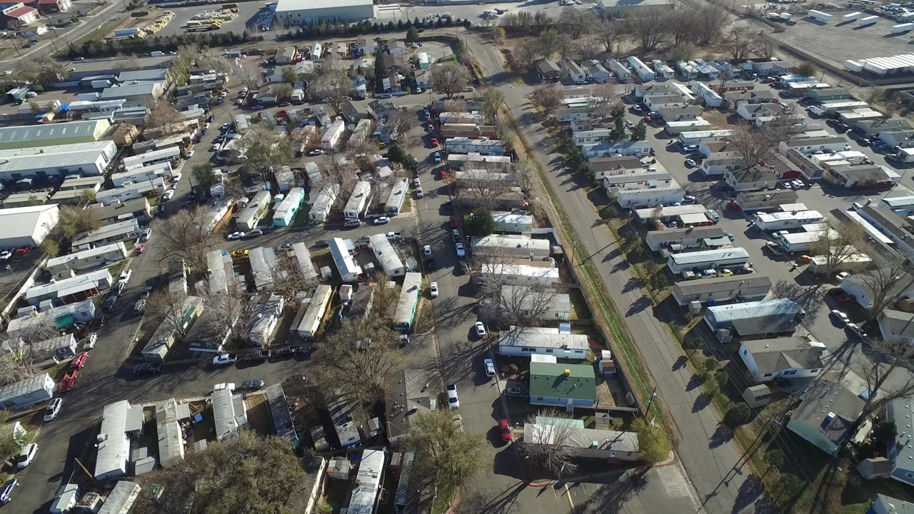 Drone-like aerial view of a residential community beside larger low buildings and parking areas.