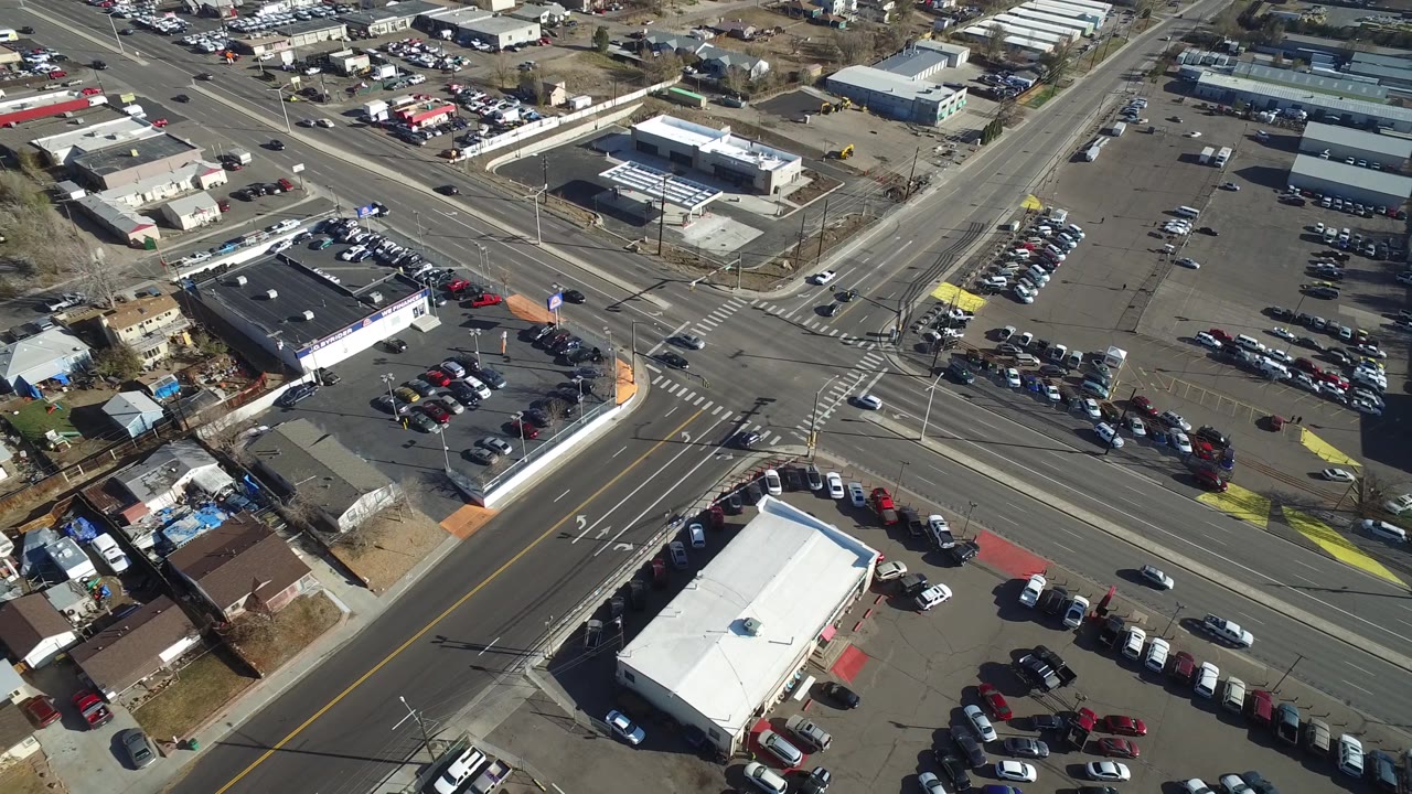 Oblique aerial view in Westminster, Colorado with the intersection shifted right, showing a white-roofed commercial building, parked vehicles, houses, and no visible people.