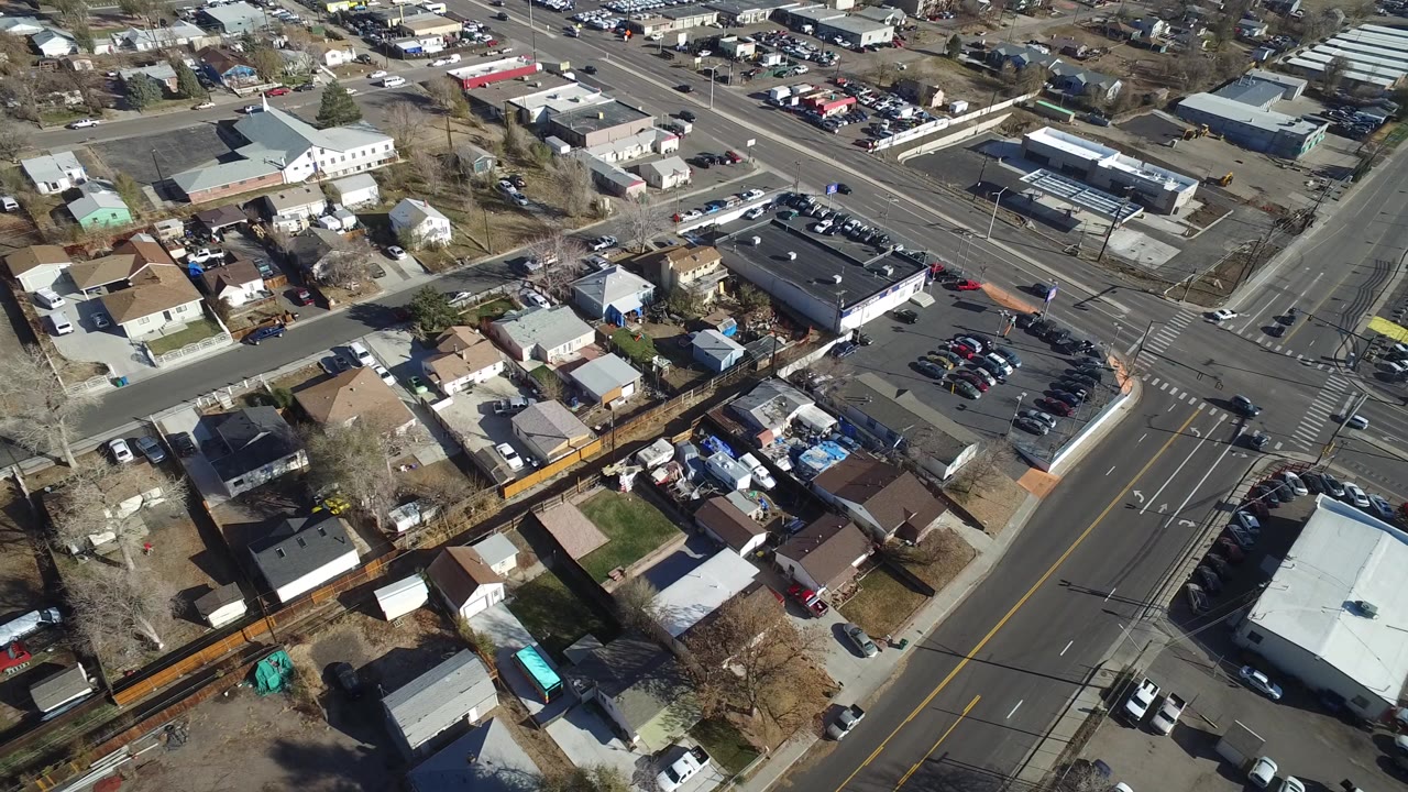 Overhead aerial view of a Westminster, Colorado neighborhood with houses, fenced yards, leafless trees, parked cars, and a broad road intersection, with no visible people.
