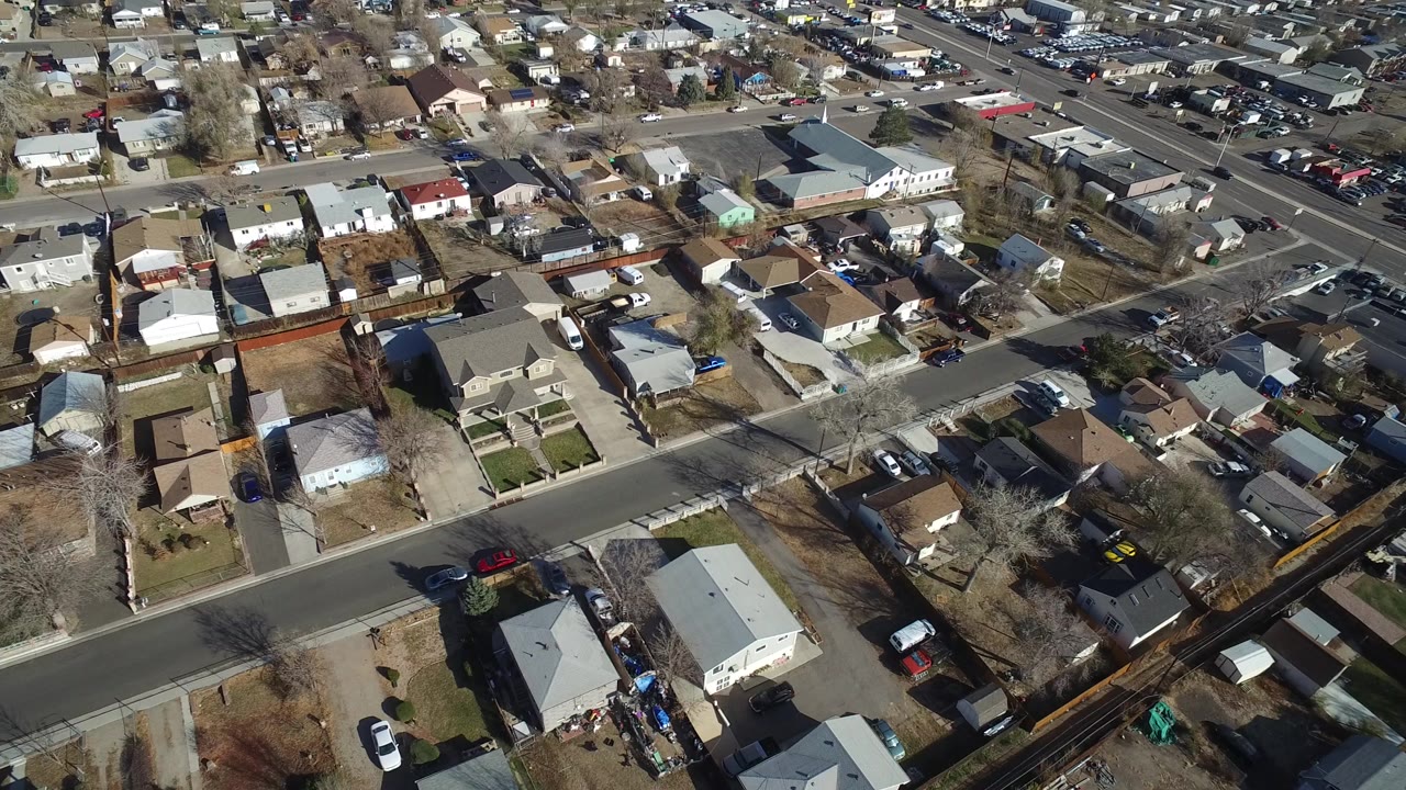 Oblique aerial view over Westminster, Colorado homes, fenced yards, parked cars, and bare trees at the start of the clip, with no visible people.