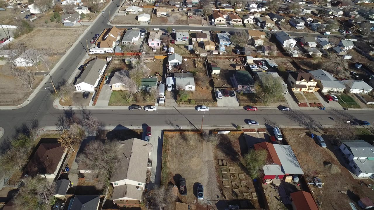 High aerial view over Westminster, Colorado homes, fenced yards, parked cars, and an intersection, with no visible people.