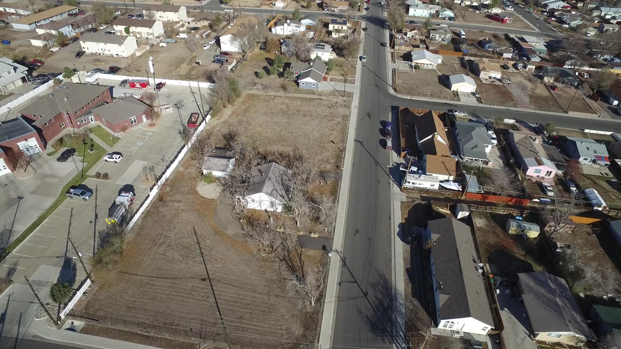 Aerial view in Westminster, Colorado with a red low-rise building, paved parking spaces, a nearby road, fenced open lot, parked vehicles, and no visible people.