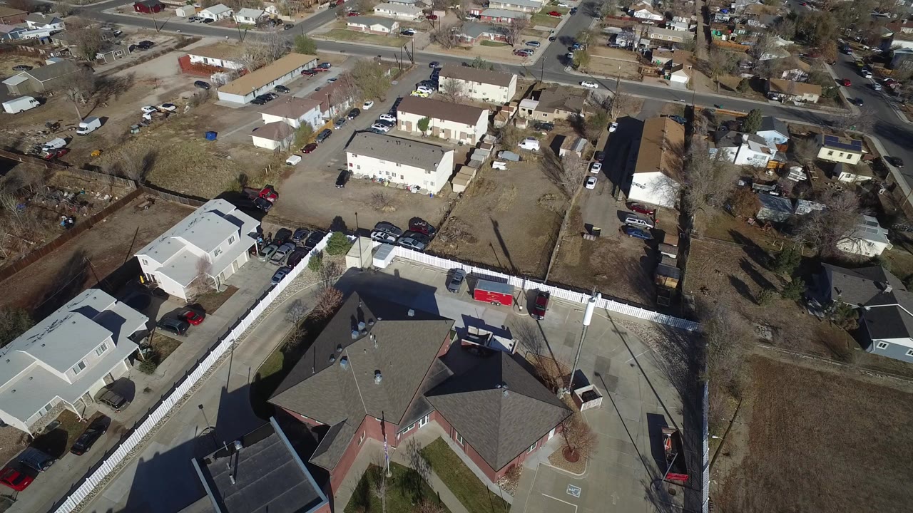 High-angle view over Westminster, Colorado homes and apartment buildings with fenced yards, bare trees, parked cars, and no visible people.