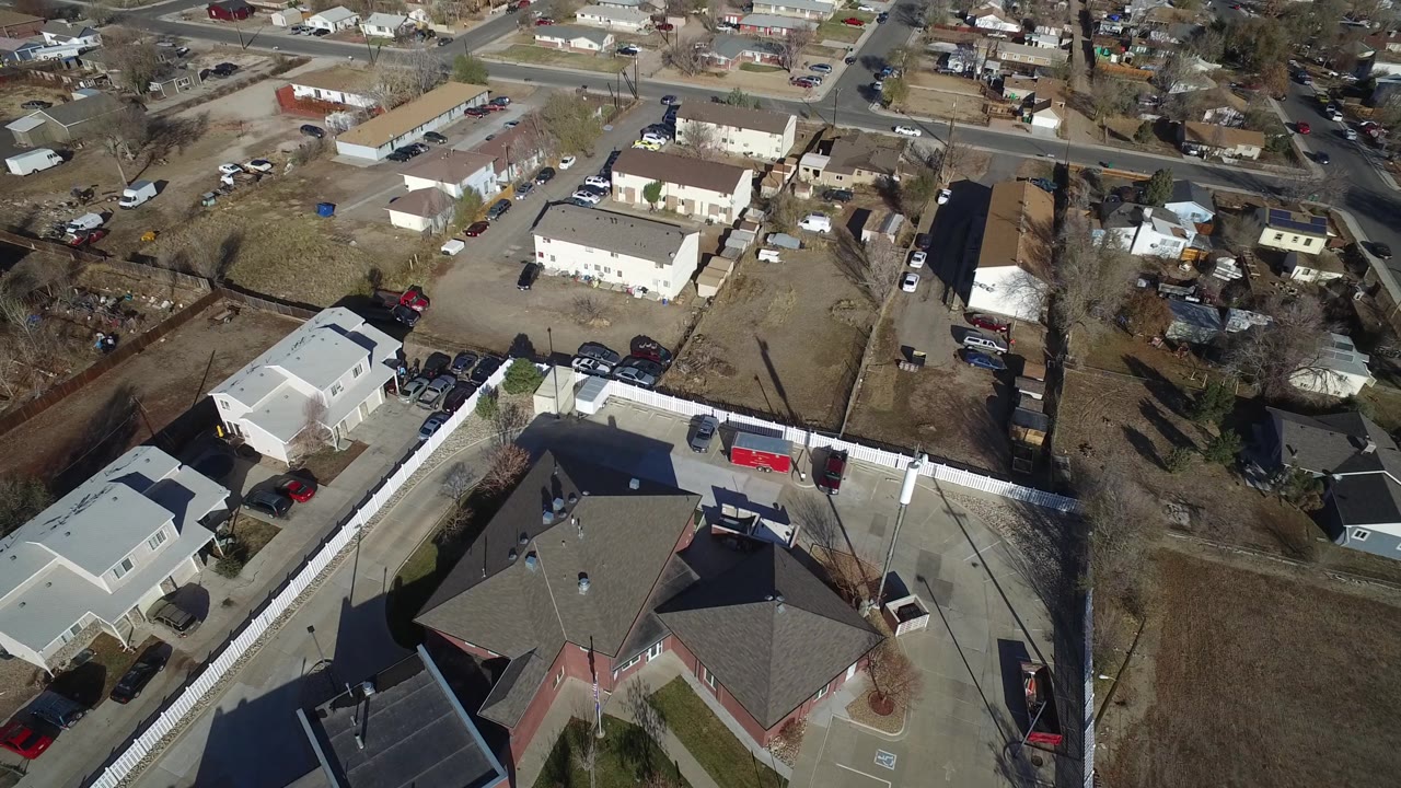 Aerial frame over Westminster, Colorado showing low-rise residential buildings, a paved parking area, a cross street, and no visible people.