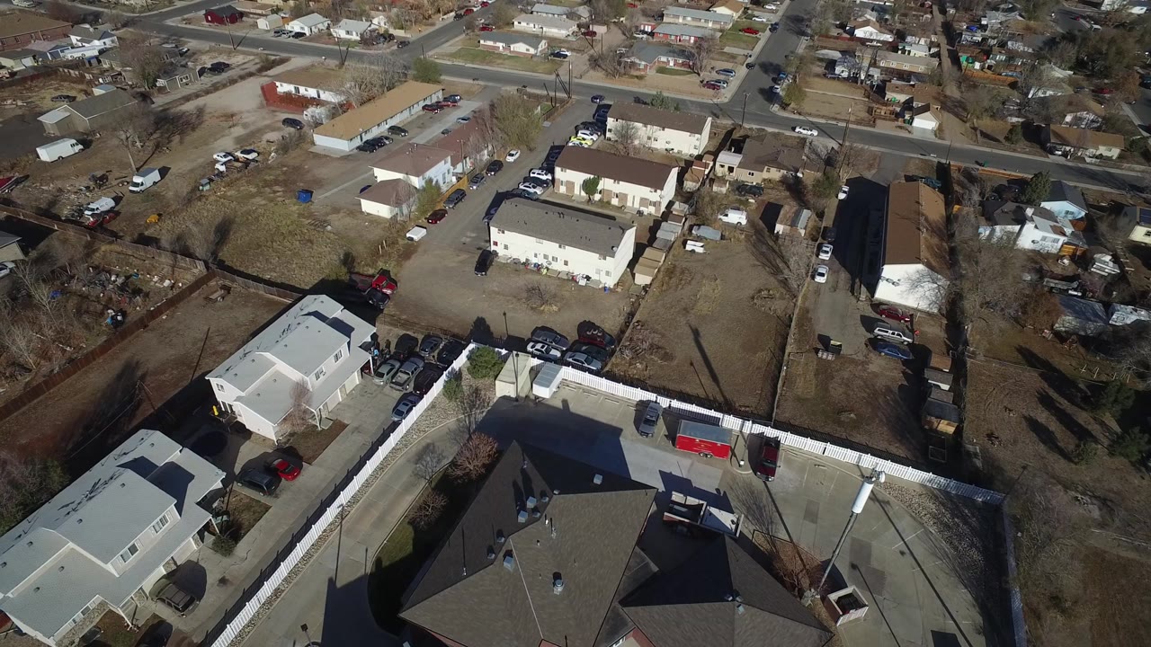 Top-down view in Westminster, Colorado with a white residential building, parked vehicles along driveways, open yards, and no visible people.