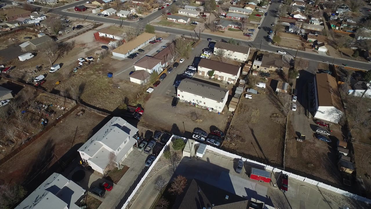 Oblique aerial view of houses, a long building, parked cars, and streets.