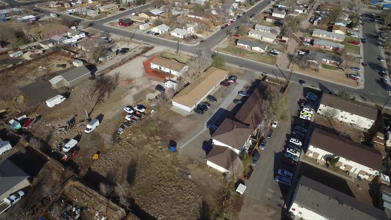 High aerial view over Westminster, Colorado homes and intersecting streets, with parked cars, bare trees, brown lawns, and no visible people.