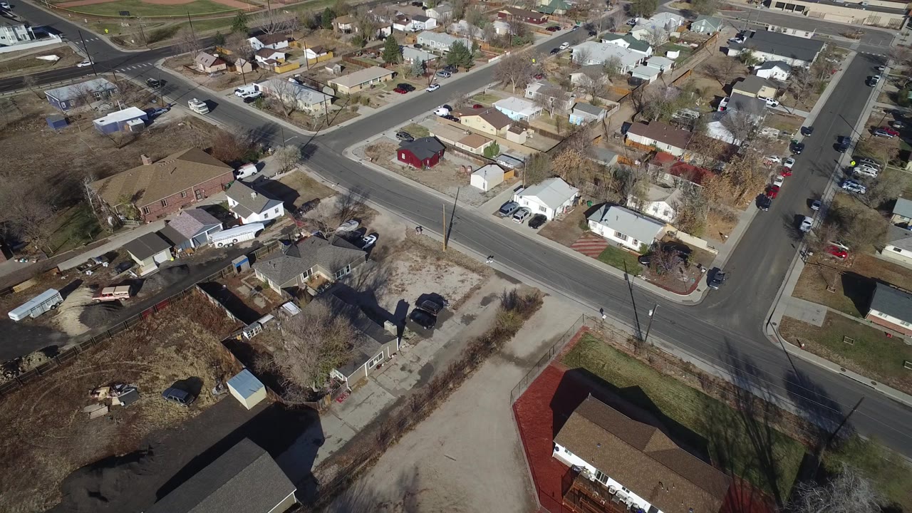 Aerial view in Westminster, Colorado with the road intersection near center, rows of homes beyond it, parked cars along streets and driveways, and no visible people.