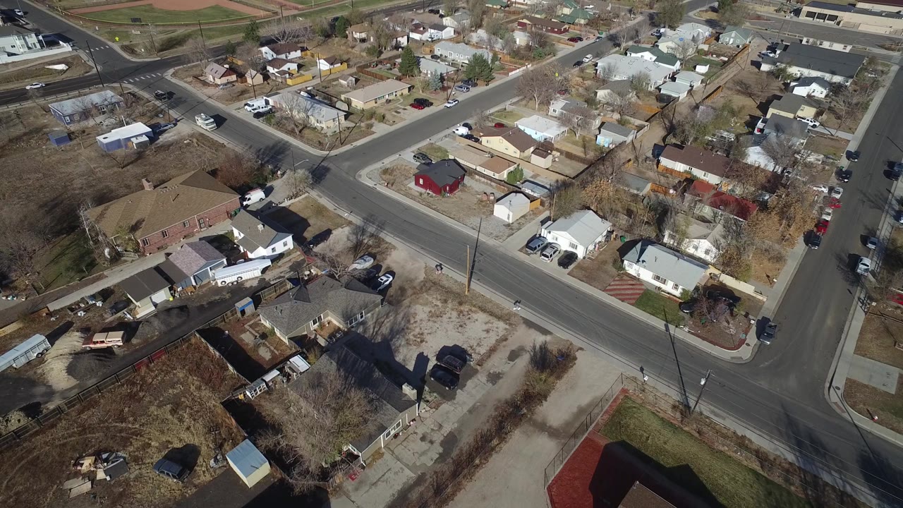 Aerial neighborhood view with a main road, houses, yards, and a sports field in the distance.