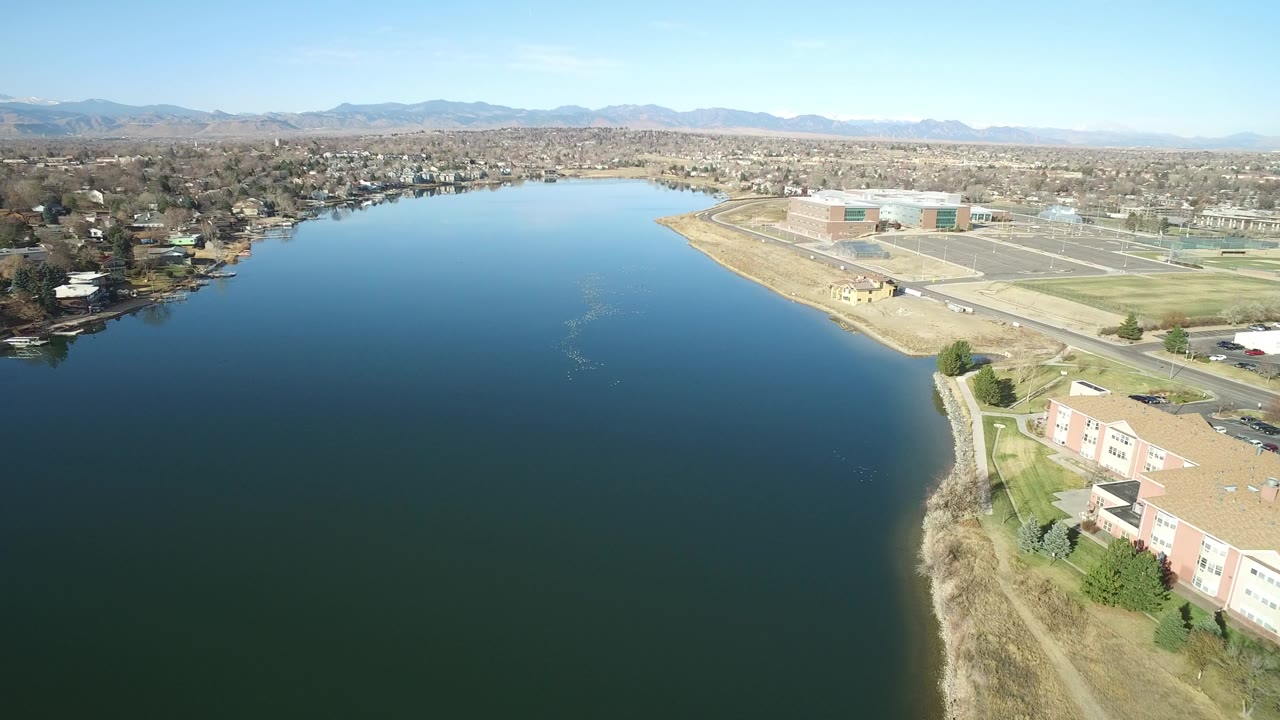 Aerial view over a deep blue lake with shoreline buildings and distant mountains.