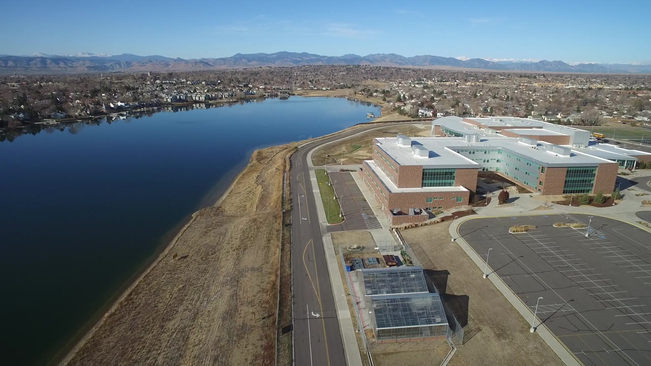 Aerial view of a lakeside office complex, road, parking lot, and distant mountains.