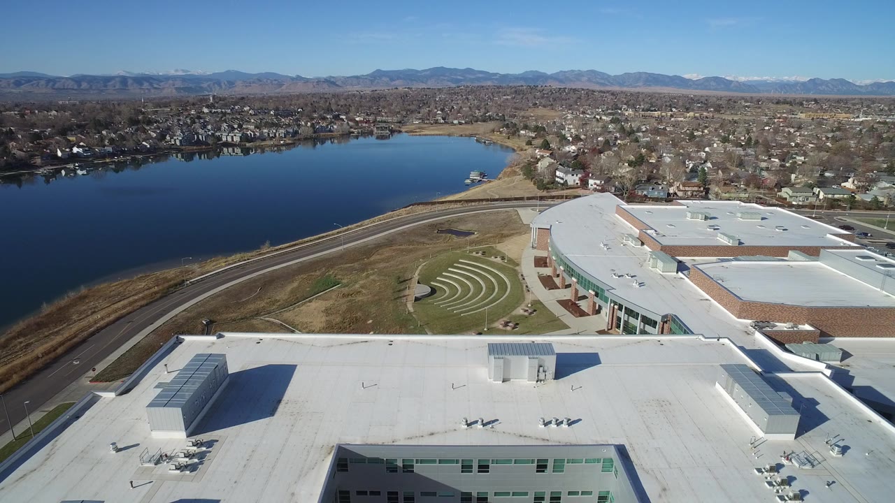Aerial view of a large white-roofed building beside water and neighborhoods.