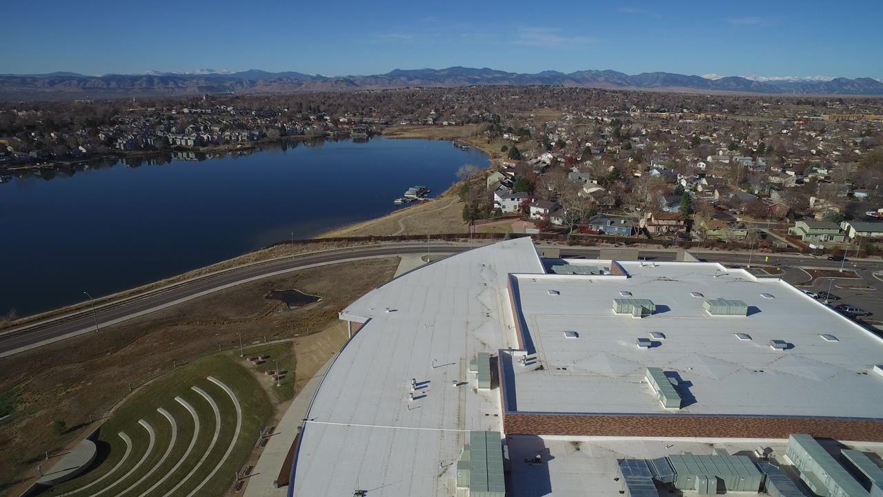 Drone-height view over a white building roof toward a lake and residential area.