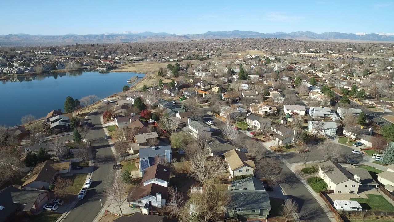Aerial view of houses, streets, lake water, and distant mountains.