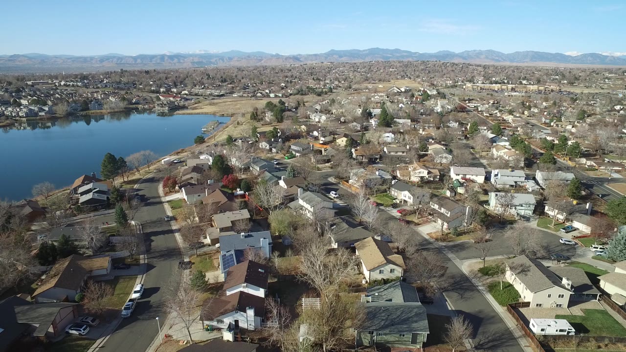 Aerial frame over Westminster, Colorado rooftops and branching streets, with the lake occupying the left side and no visible people in the scene.