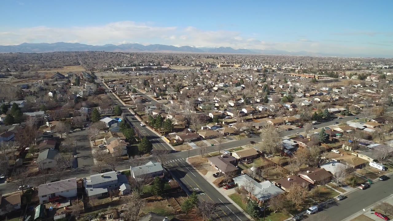 Wide aerial frame over Hidden Lake, Colorado houses and intersecting roads with distant mountains under a clear blue sky, no visible people.