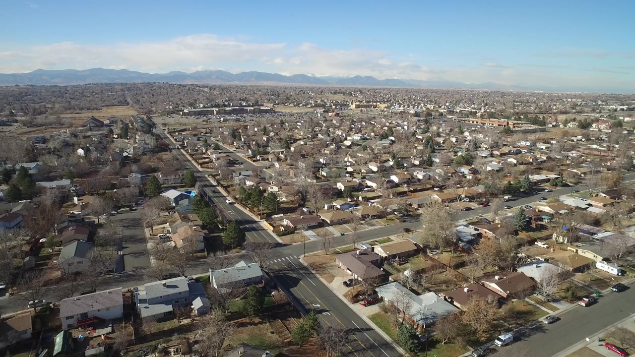 Elevated view of Hidden Lake, Colorado rooftops and a long straight road running through the neighborhood toward low mountains, no visible people.
