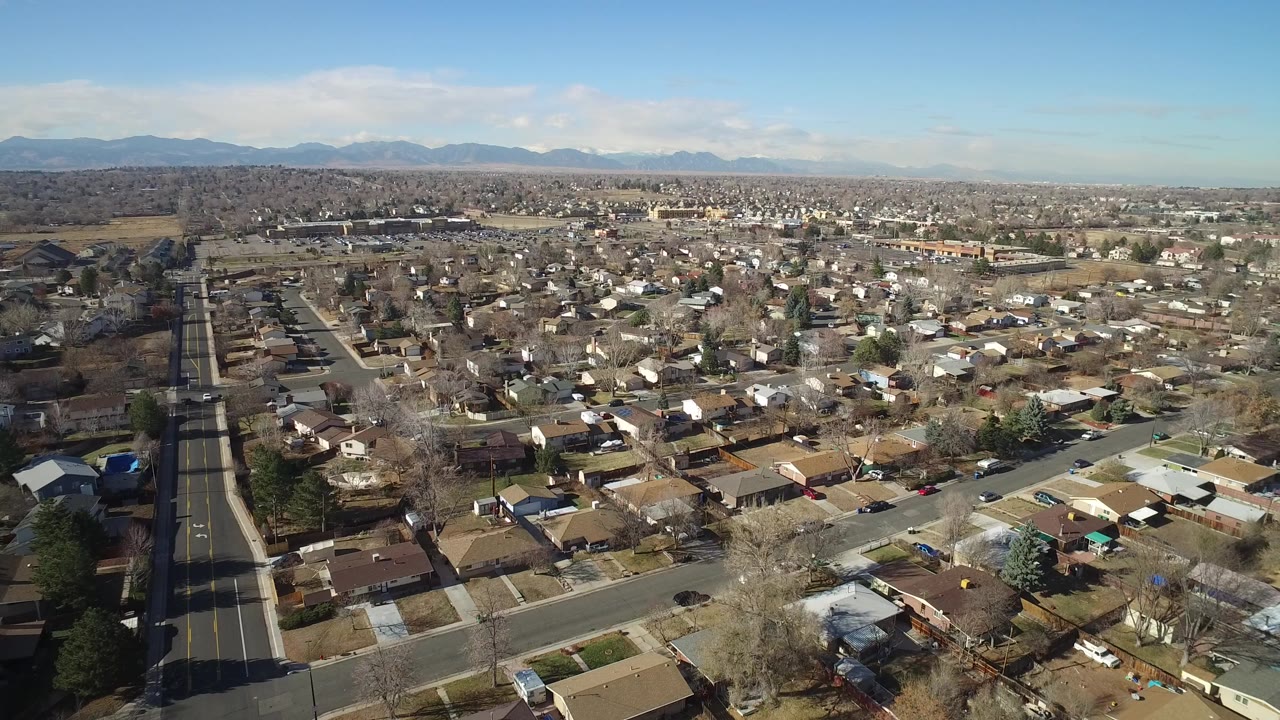 Aerial view over suburban homes with streets and distant mountains.