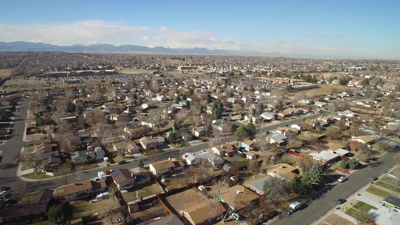 High aerial view over Hidden Lake, Colorado homes, curving streets, bare trees, and a distant mountain horizon under clear daylight, with no visible people.