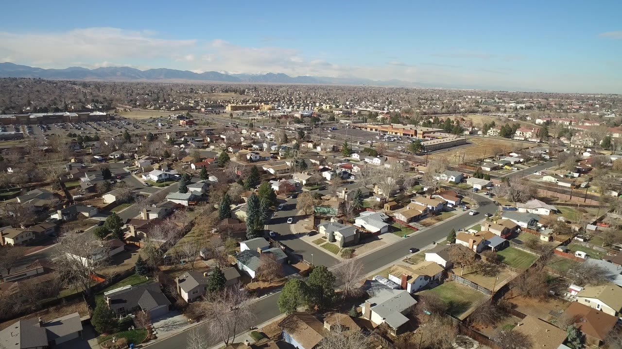 Hidden Lake, Colorado residential blocks spread across the frame, with quiet streets, small yards, scattered parked vehicles, and a low mountain range along the horizon.