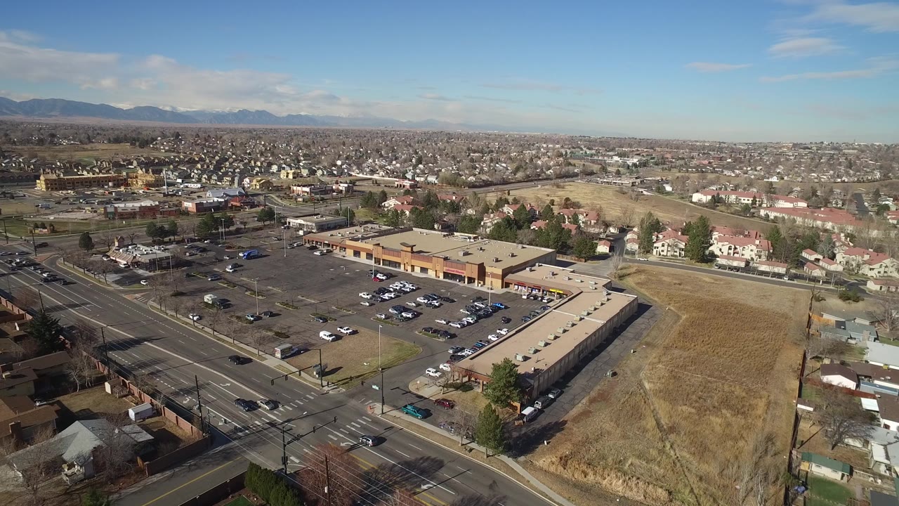 Aerial frame with a parking lot, low commercial building, roads, homes, and mountains.