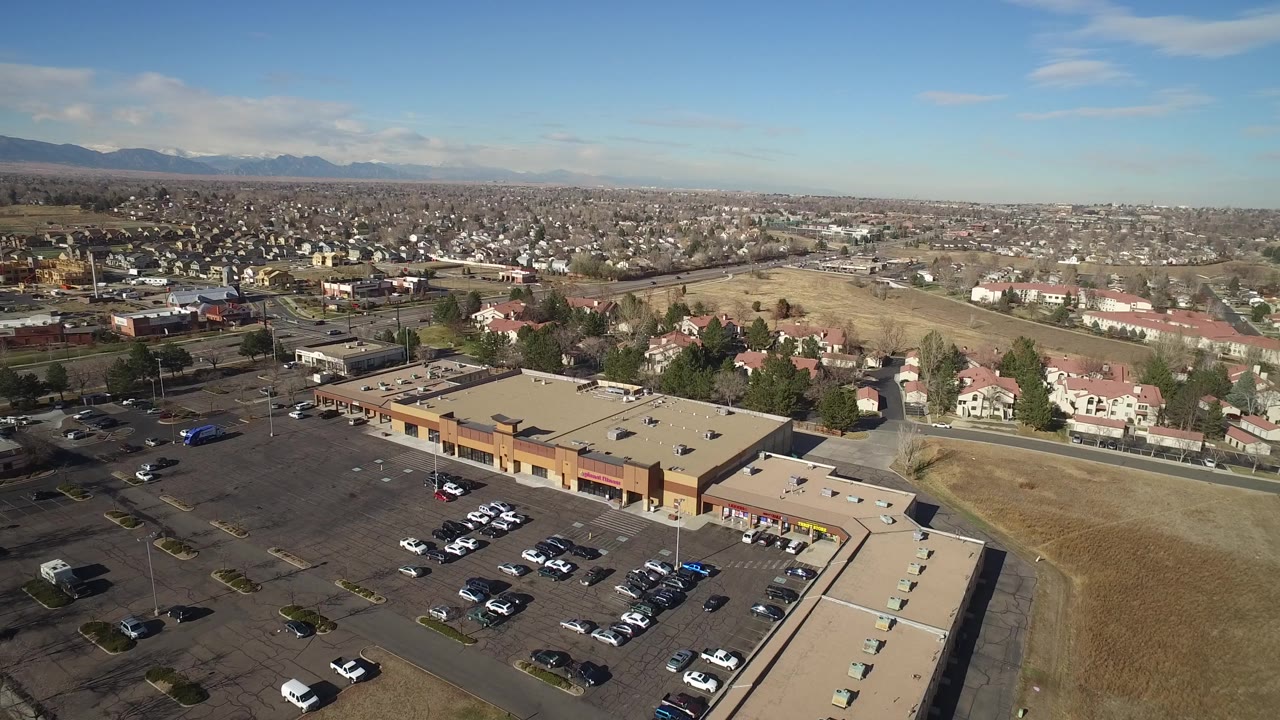 Aerial frame in Hidden Lake, Colorado with the tan retail roof and rows of parked cars below, residential streets behind, and no visible people.