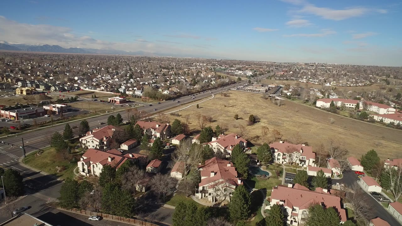 High aerial view over red-roofed homes, roads, open field, and distant mountains
