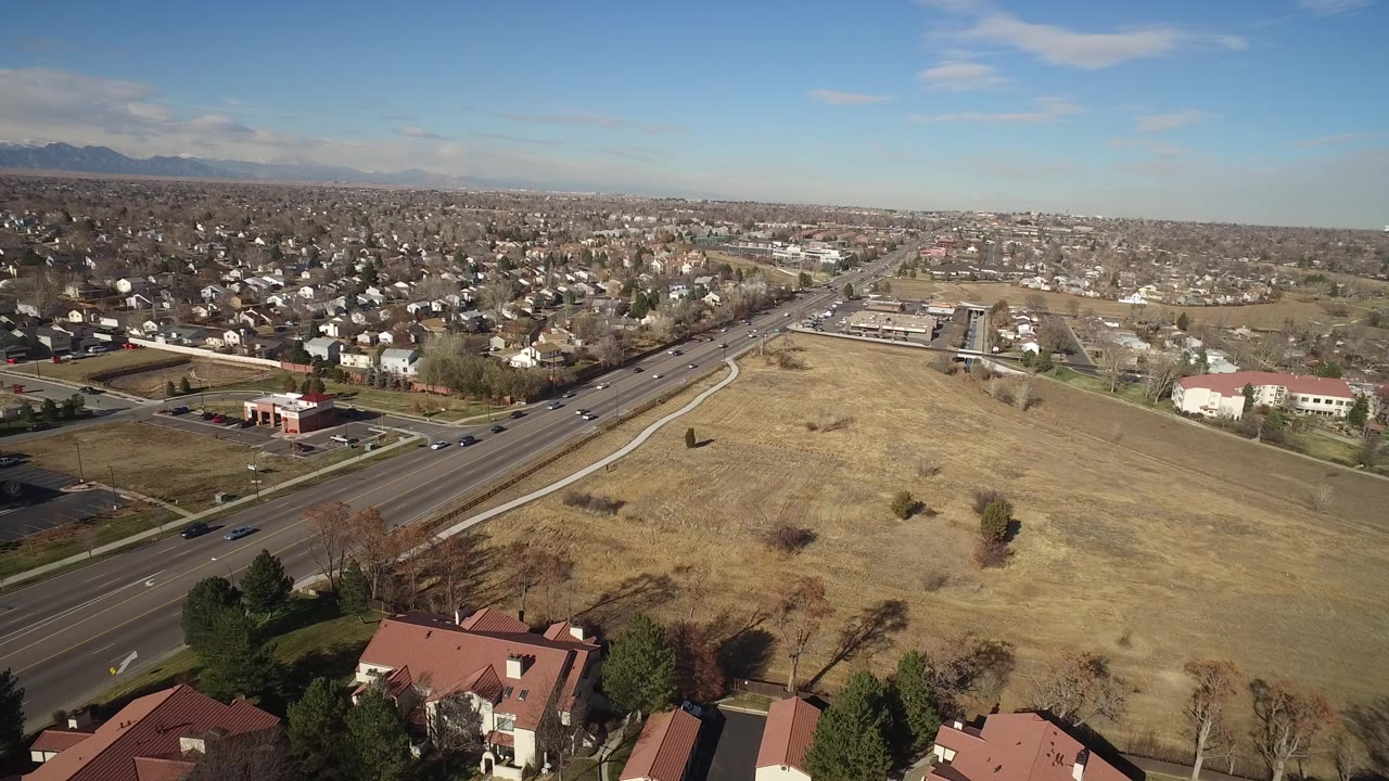 Wide aerial of residential blocks, commercial buildings, road, and dry grassland.