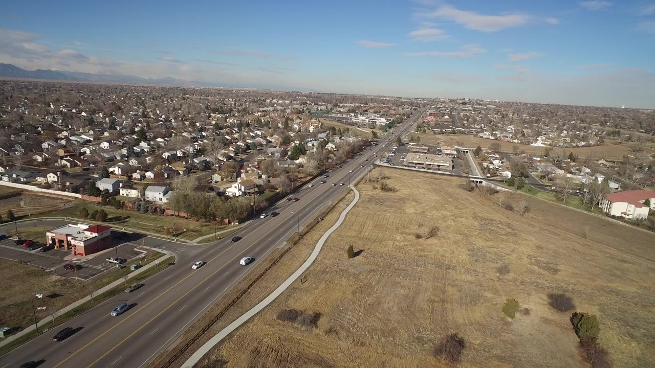 Aerial view of a road beside open field and suburban homes.