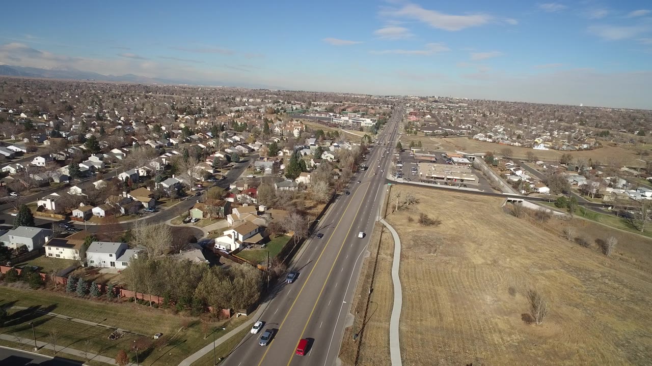 Aerial view in Hidden Lake, Colorado with the main road centered, a red vehicle near the lower road, residential streets to the left, open land to the right, and no visible people.