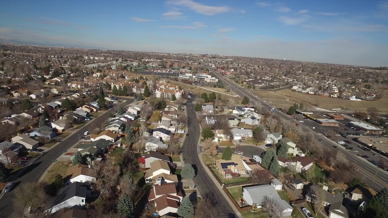 Aerial view of houses, roads, open grass, and a wide suburban horizon.